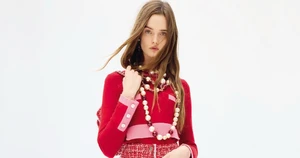 Model Lulu Tenney wearing a red knit top and layered pearl necklaces against a white background for Chanel.