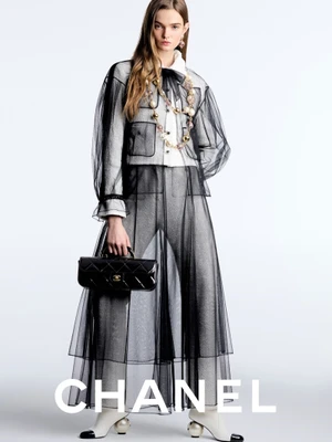 Model Lulu Tenney wearing a black sheer tulle jacket over trousers, holding a quilted handbag against a white background for Chanel.