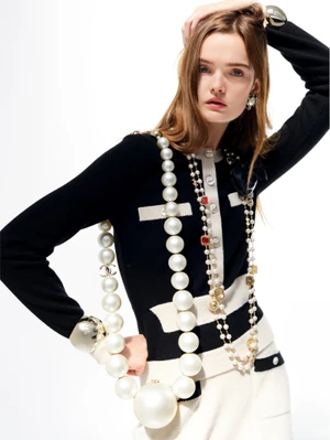 Model Lulu Tenney wearing Chanel knitwear layered with oversized pearl necklaces and silver cuffs against white background
