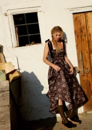 Dorit Revelis wearing patterned dress and clogs outside white rustic building for For Love & Lemons Fall 2025 campaign