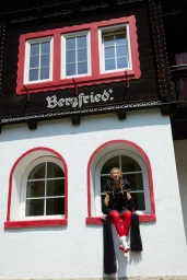 Model Dorit Revelis sitting in a white arched window wearing a black dress and red tights for For Love & Lemons