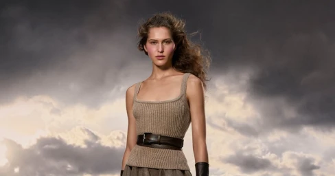 Angelina Kendall wearing a ribbed knit tank top and dark belt against a dramatic stormy sky background.