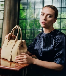 Scarlett Johansson holding a beige Prada handbag in front of a dark window frame, photographed by Yorgos Lanthimos.