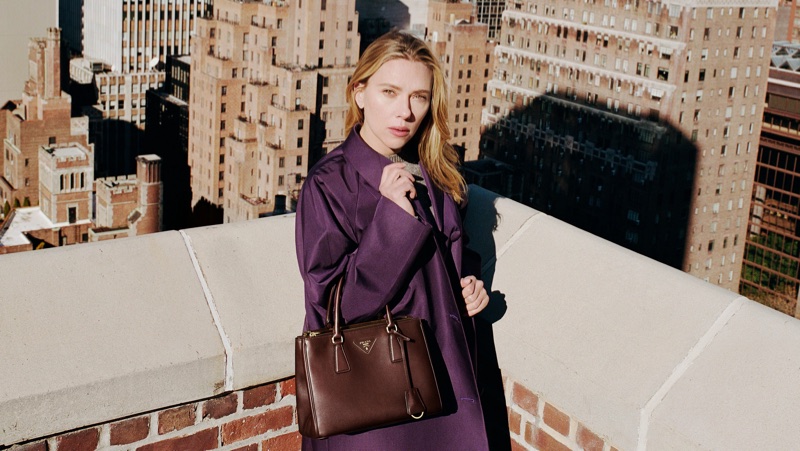 Scarlett Johansson wearing a purple coat on a rooftop holding a brown leather handbag, photographed by Yorgos Lanthimos.