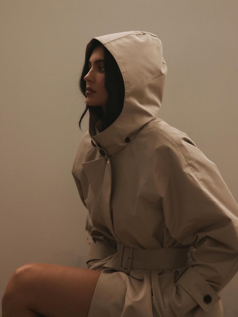 Kylie Jenner wearing a beige hooded belted trench coat against a neutral studio backdrop for the Khy x HYDRA capsule collection.