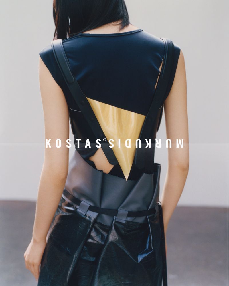 Fashion shot featuring a woman from the back wearing a modern black dress with angular design elements and a golden triangular cutout.