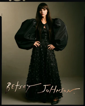 Christina Ricci wearing a black dress with oversized sleeves against a neutral backdrop for Betsey Johnson