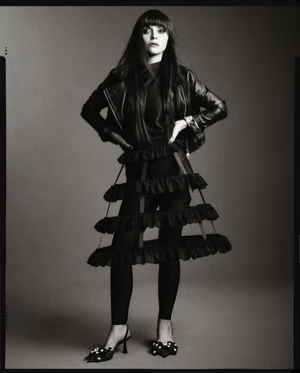 Christina Ricci in a black leather jacket and tiered cage skirt standing against a grey studio backdrop.