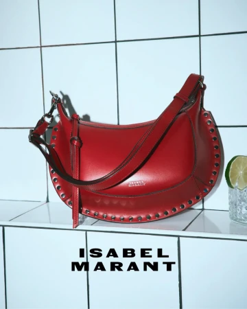 Red leather studded shoulder bag resting on a white ceramic tiled shelf beside a cocktail glass with a lime wheel.