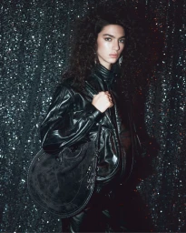 Model Loli Bahia in a black leather jacket holding a suede handbag against a glittering dark backdrop for Isabel Marant