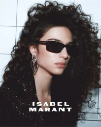 Model with voluminous dark curly hair wearing black sunglasses and large heart earrings in Isabel Marant campaign