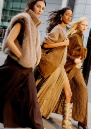 Four female models walking outdoors in stylish autumn apparel including fur vests and pleated skirts for an H&M campaign.