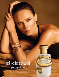 Model Natasha Poly posing with a Roberto Cavalli Serpentine fragrance bottle on a rustic wooden surface.