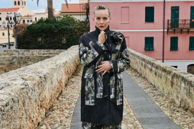 Sharon Stone wearing a patterned black coat standing on a stone pathway for the Antonio Marras Fall-Winter 2025 campaign.