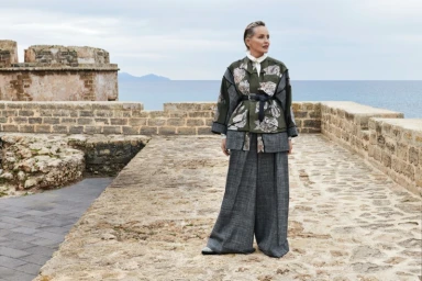 Sharon Stone wearing floral patterned jacket and wide trousers standing on a stone terrace overlooking the sea