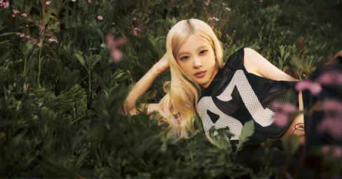 ROSÉ lying in tall green grass wearing a black mesh athletic top with white graphic numbers for PUMA