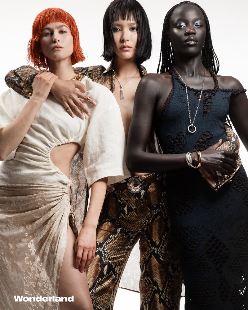 Three diverse women pose in a studio shot with contrasting patterned outfits and jewelry, showcasing a fashion editorial style.