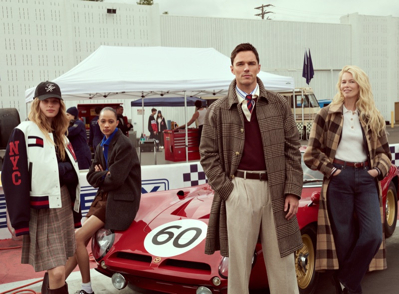 Nicholas Hoult, Claudia Schiffer, and models posing with a vintage red race car in a paddock for Tommy Hilfiger.