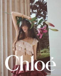 Model Grace Hartzel holding a flowering lily branch against a stone column for Chloé Winter 2025 campaign.