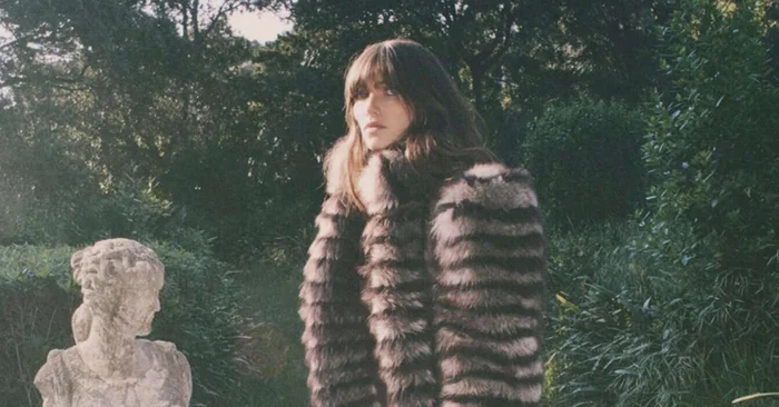 Grace Hartzel wearing a patterned fur coat in a garden with a stone statue for Chloé Winter 2025 campaign by David Sims