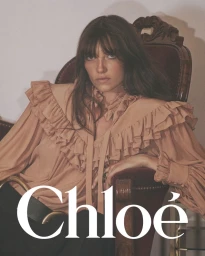 Model Grace Hartzel seated in a vintage armchair wearing a ruffled beige blouse for Chloé Winter 2025 campaign