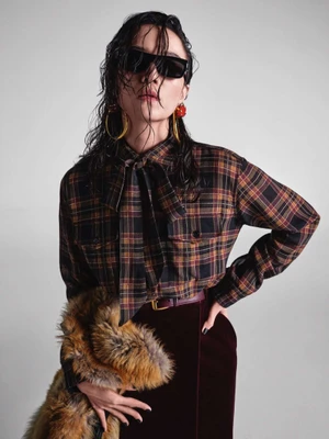Model with wet hair wearing sunglasses, plaid shirt, and velvet skirt for Yves Saint Laurent Fall 2025 campaign