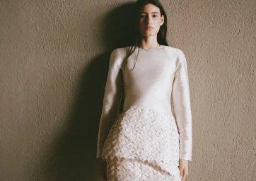 Model standing against a textured wall wearing a cream-colored long-sleeve dress with patterned skirt from H&M and Lorena Saravia.