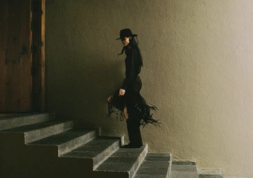 Model wearing black fedora hat and fringe skirt walking up stone stairs