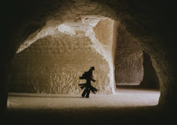 Model wearing dark fringe clothing inside a natural stone cave or cavern formation.