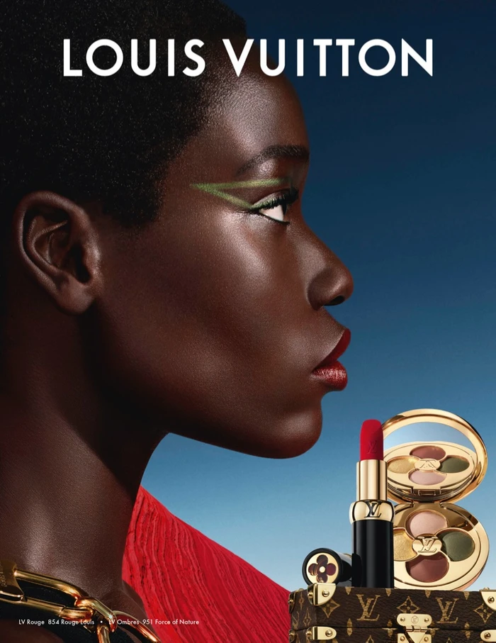 Close-up profile portrait of a black woman wearing vibrant green eyeliner and red lipstick for Louis Vuitton cosmetics.