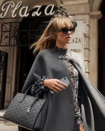 Model in grey cape holding a patterned handbag and smartphone outside a hotel entrance