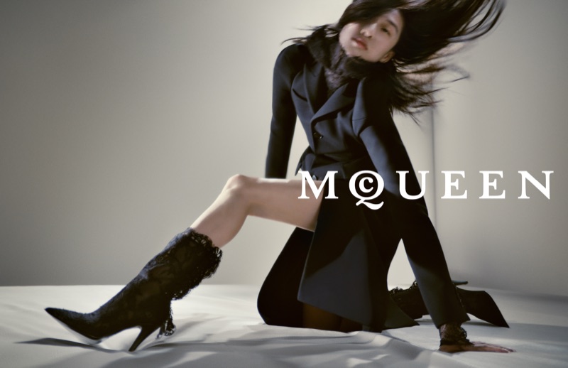 Chu Wong poses dynamically in a black tailored coat and lace boots for the Alexander McQueen Fall-Winter 2025 campaign.