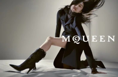 Model in black jacket and lace boots with hair whipping across a white backdrop for Alexander McQueen