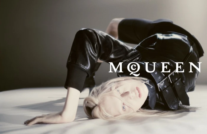 Model in black leather jacket arching backwards on a white seamless backdrop with overlaid McQueen logo