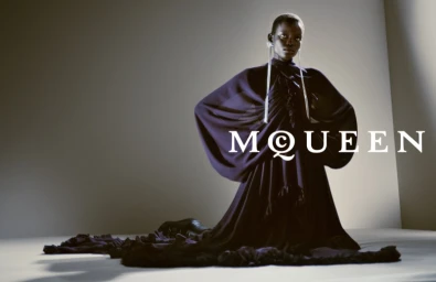 Model kneeling in a dark draped gown against a plain background with overlaid text for Alexander McQueen