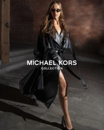 Model Angelina Kendall in dark sunglasses and a black leather coat walking past a brick wall