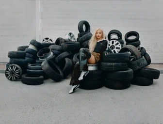 ROSÉ seated on a large pile of black car tires against a grey wall for Puma Metallic Speedcat campaign