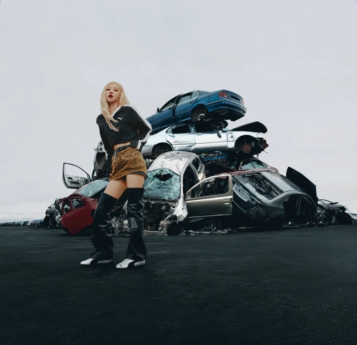 ROSÉ posing in front of a large pile of wrecked cars in a Puma Metallic Speedcat campaign image