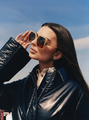 Emily Ratajkowski wearing tortoiseshell sunglasses and a black leather jacket against a clear blue sky for Tory Burch.