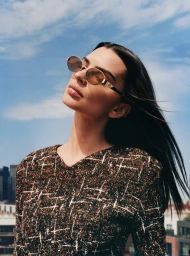 Emily Ratajkowski wearing oval sunglasses and a tweed top against a blue sky for Tory Burch Fall-Winter 2025 Eyewear Campaign