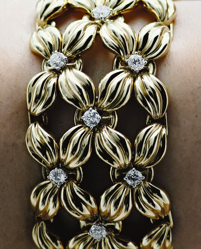 Close-up shot of a gold bracelet with white gemstones on a woman's wrist. The bracelet features a floral motif pattern.