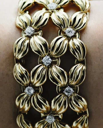 Close-up shot of a gold bracelet with white gemstones on a woman's wrist. The bracelet features a floral motif pattern.