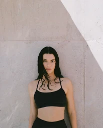 Kendall Jenner wearing black activewear standing against a concrete wall for Alo