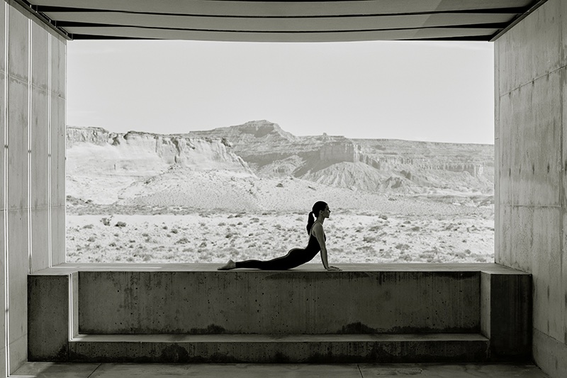 Kendall Jenner doing yoga in black activewear on a concrete ledge framing a desert mountain landscape for Alo Luxury Is Wellness