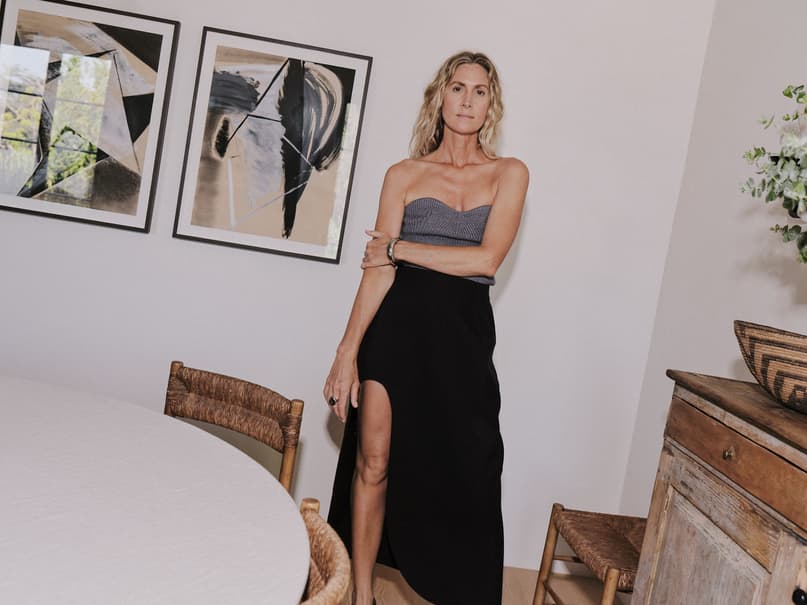 Jessica de Ruiter standing in a strapless top and high-slit black maxi skirt beside a dining table with framed wall art.