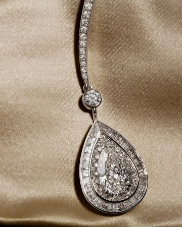 Close-up of a Boucheron teardrop diamond pendant necklace featuring a pear-cut center stone on draped champagne silk fabric.