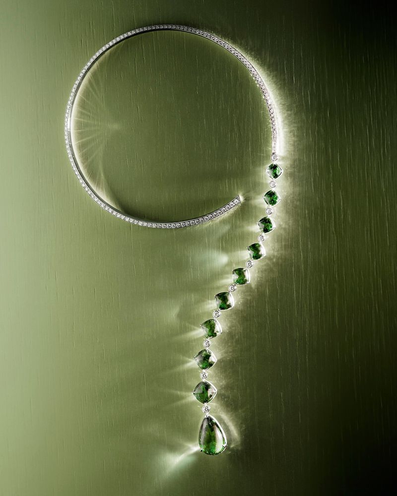 Boucheron diamond and graduated green gemstone question mark collar necklace resting on a textured olive green surface.