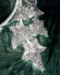Close-up of diamond-encrusted ivy leaf jewelry set against a dark green veined marble surface.