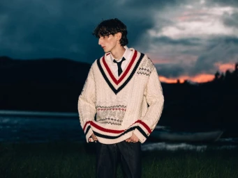 Arthur del Beato wearing an oversized cream striped cable-knit sweater and tie outdoors at dusk against a moody twilight sky.
