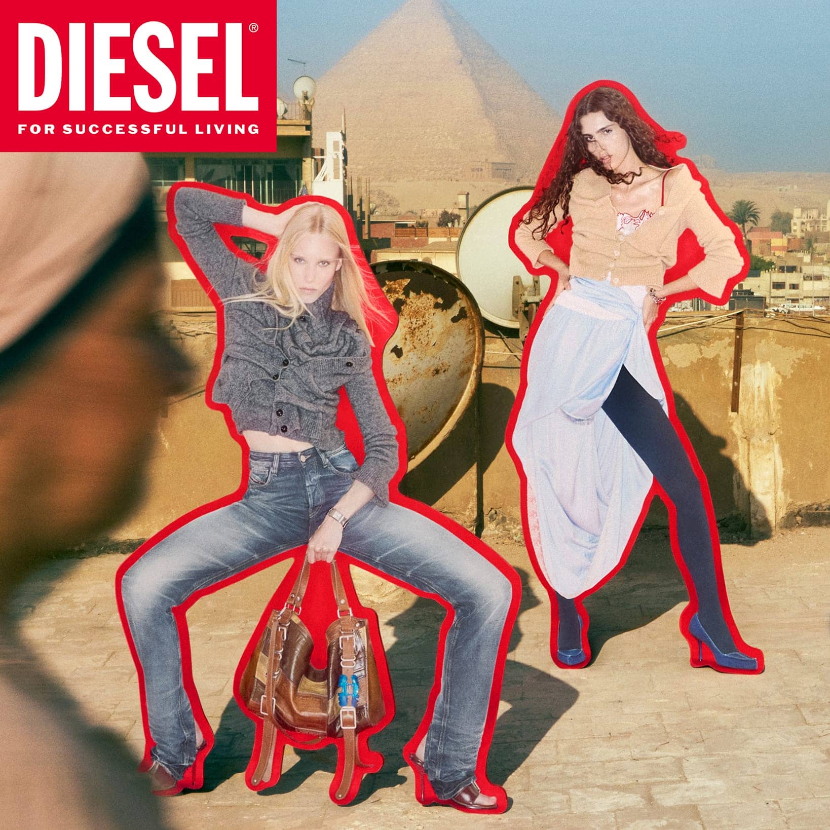 Two fashion models with red sticker outlines posed on a rooftop with a pyramid in the background for a Diesel campaign.